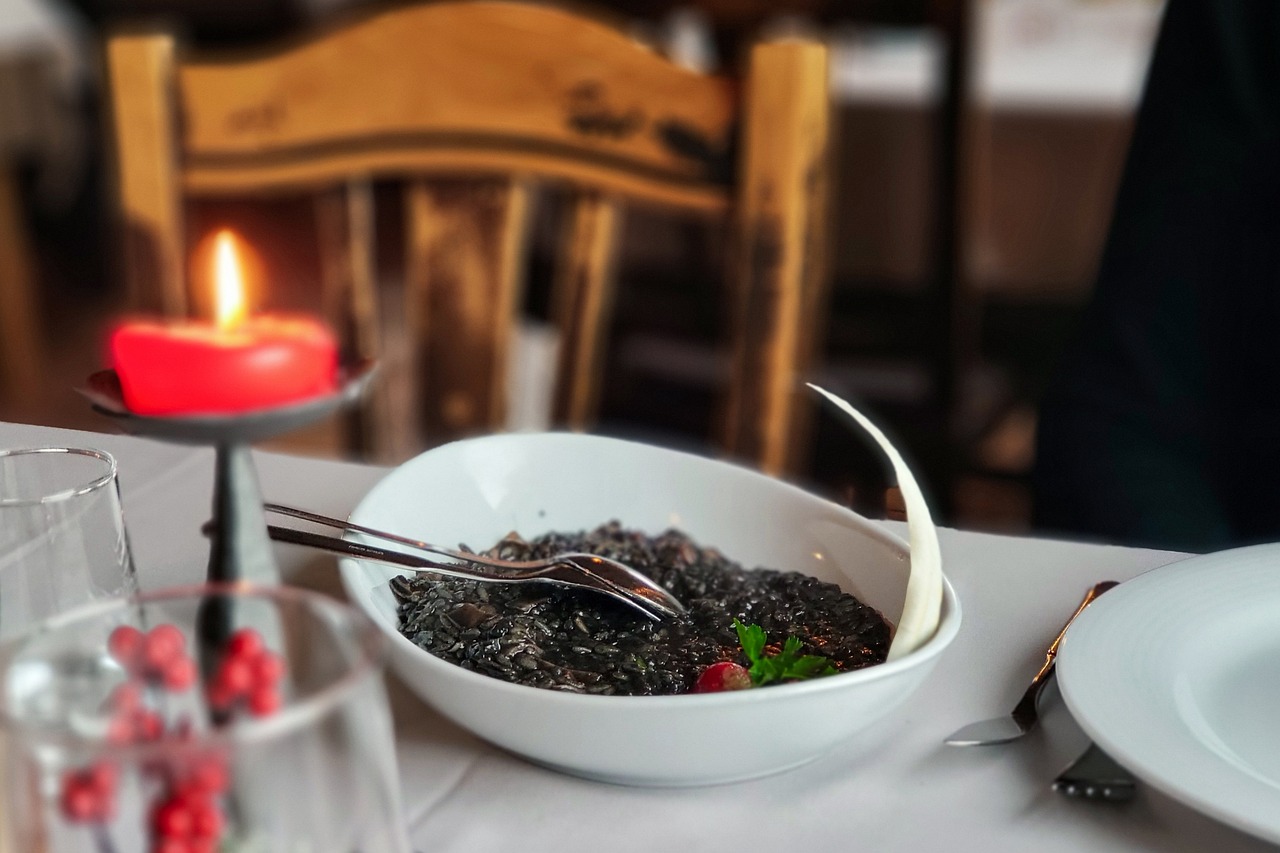 Home black risotto, squid ink risotto, gourmet dish, candlelit dinner, cozy restaurant, romantic meal, seafood risotto, fine dining, holiday ambiance, elegant plating, rustic setting, festive dinner, romantic table, italian cuisine, food presentation, dinner setting, warm atmosphere, culinary art, red candle, festive decor, gourmet experience, romantic mood, restaurant table, cozy evening, winter dinner