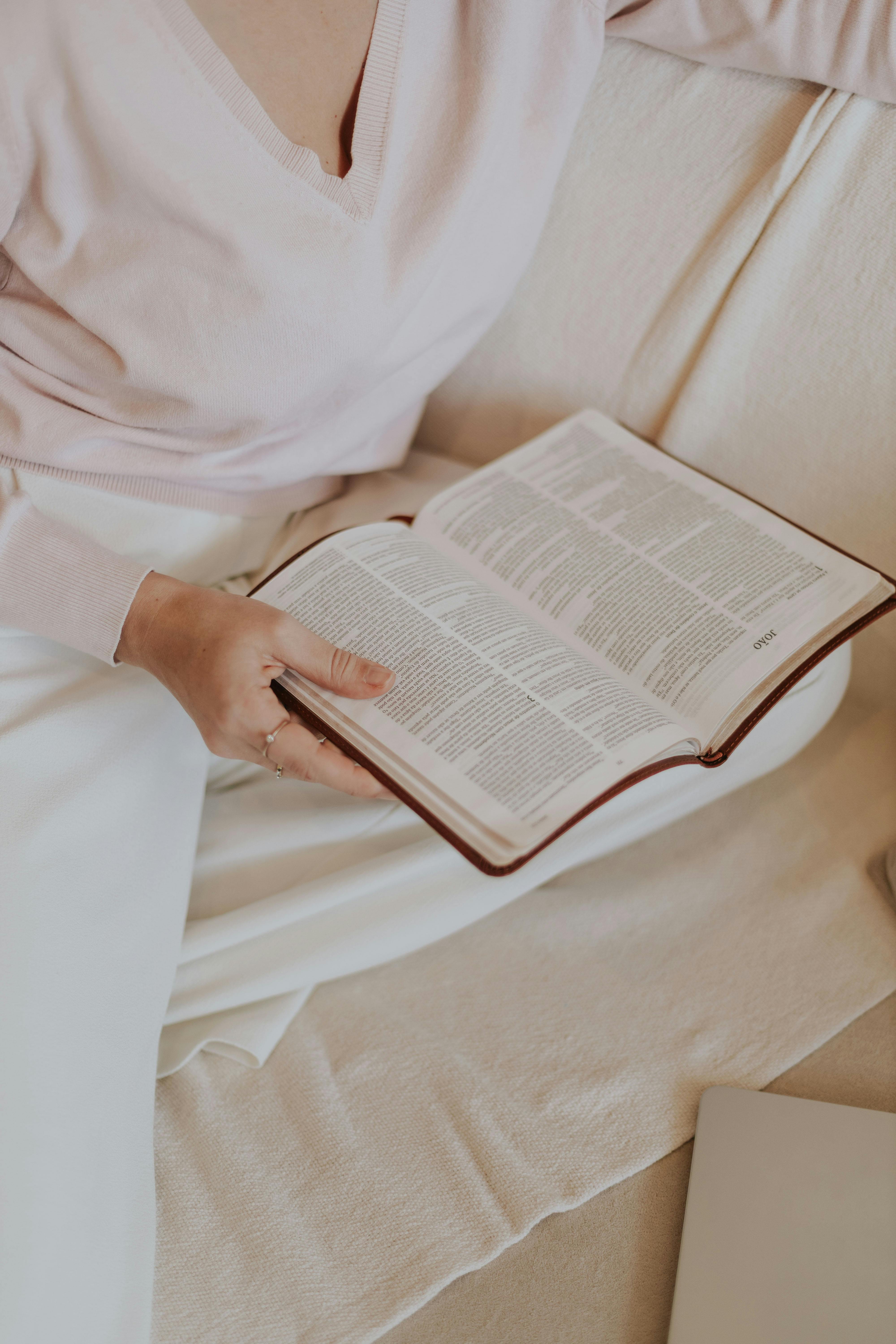 A woman in a pink sweater reading a book on a beige sofa, creating a cozy and relaxed atmosphere.