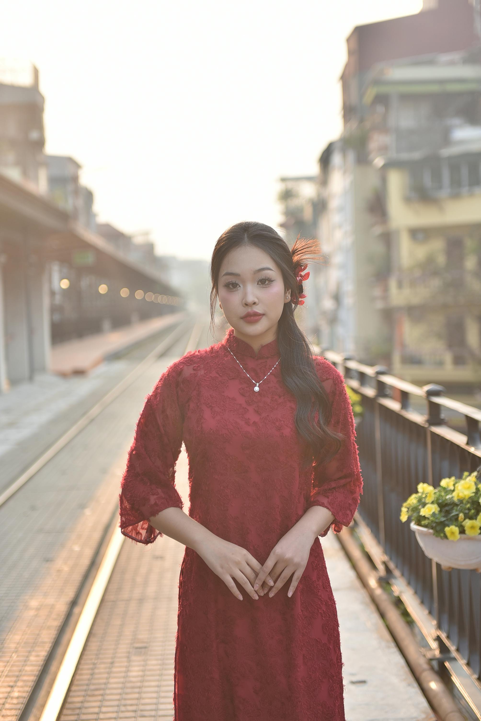 Woman in a red dress stands confidently in an urban setting during sunset.