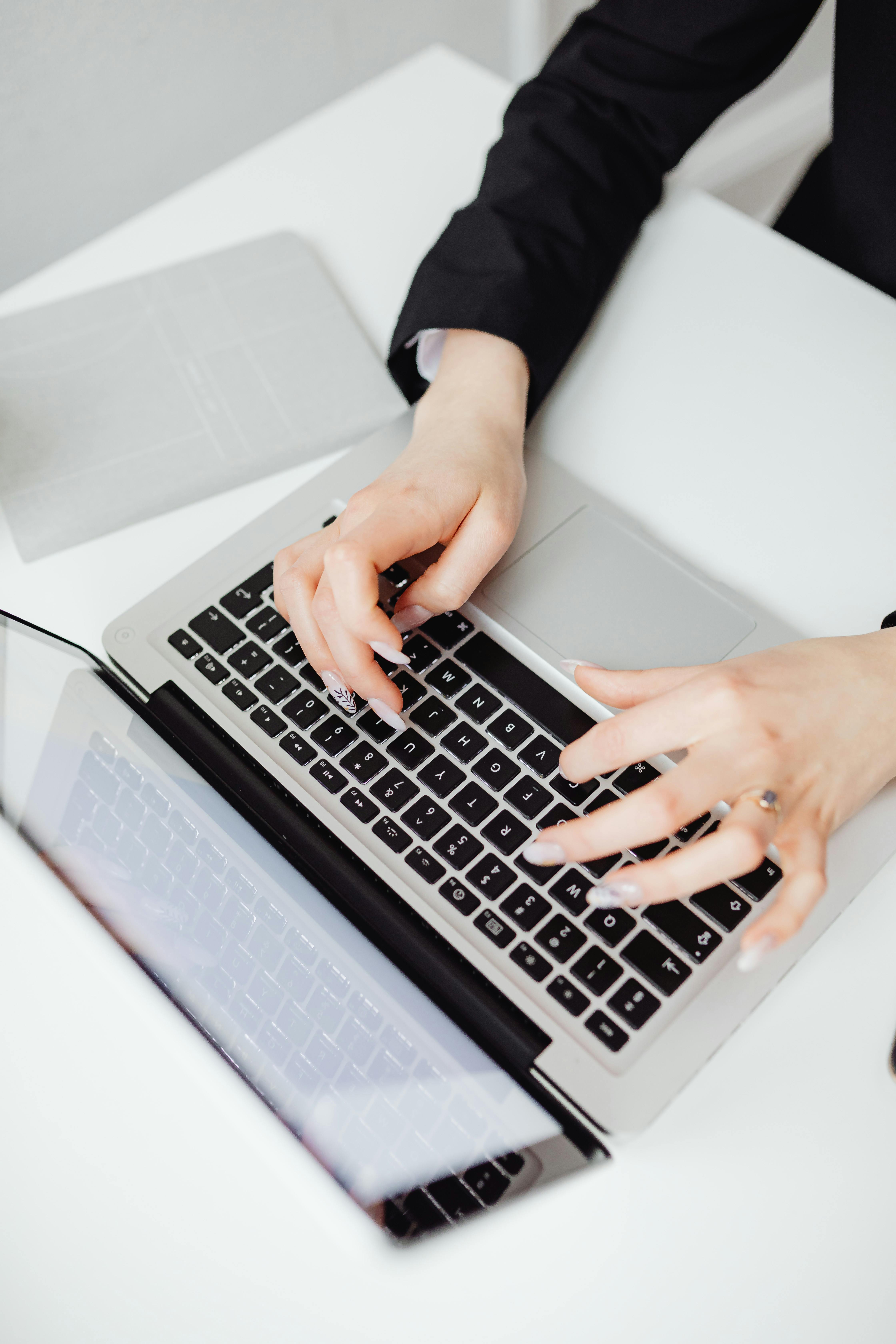Hands typing on a laptop keyboard on a white desk in an office setting.