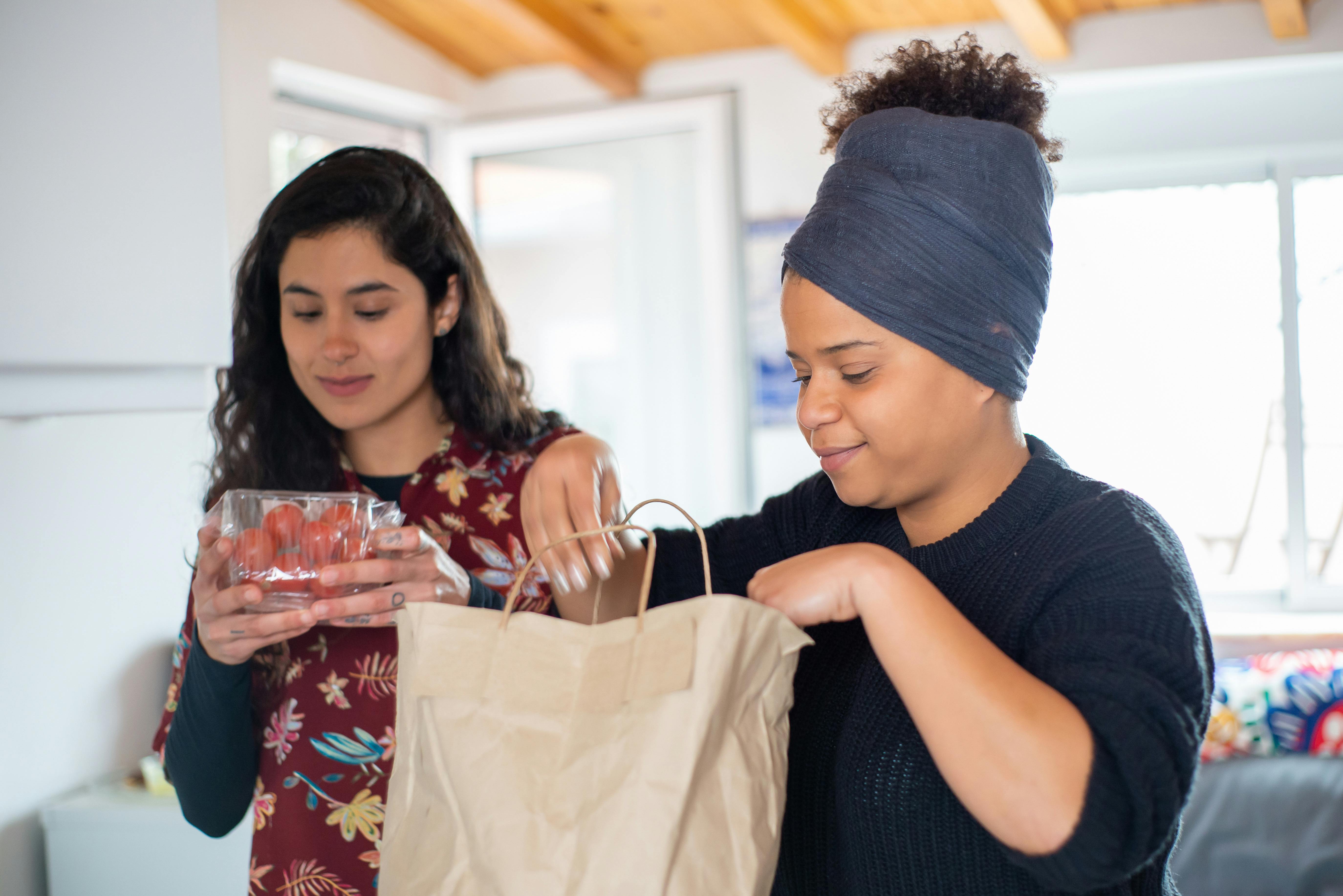 Two women joyfully unpack groceries at home, showcasing love and togetherness.