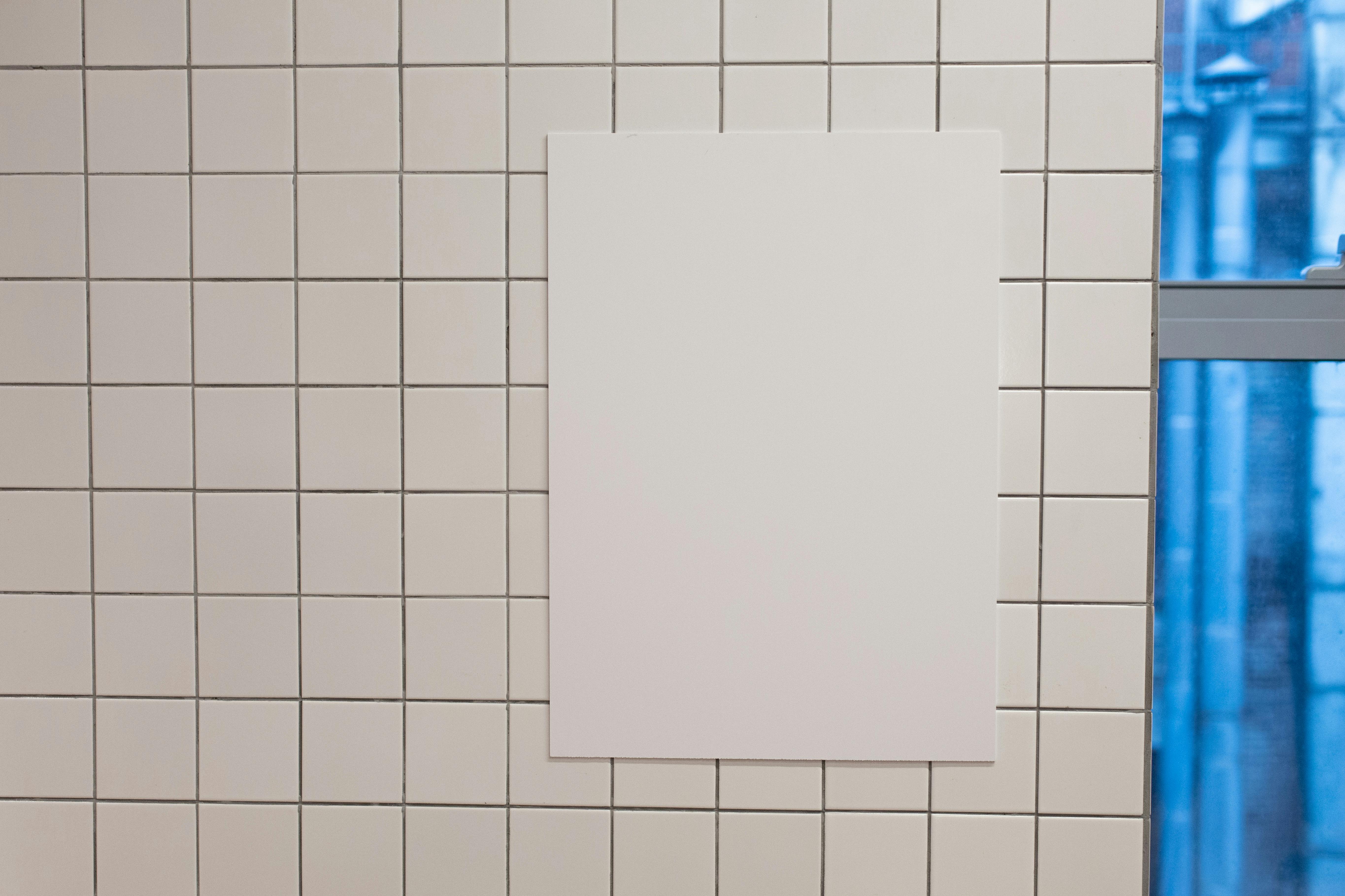 Blank white placard hanging on wall covered with white tiles inside of building