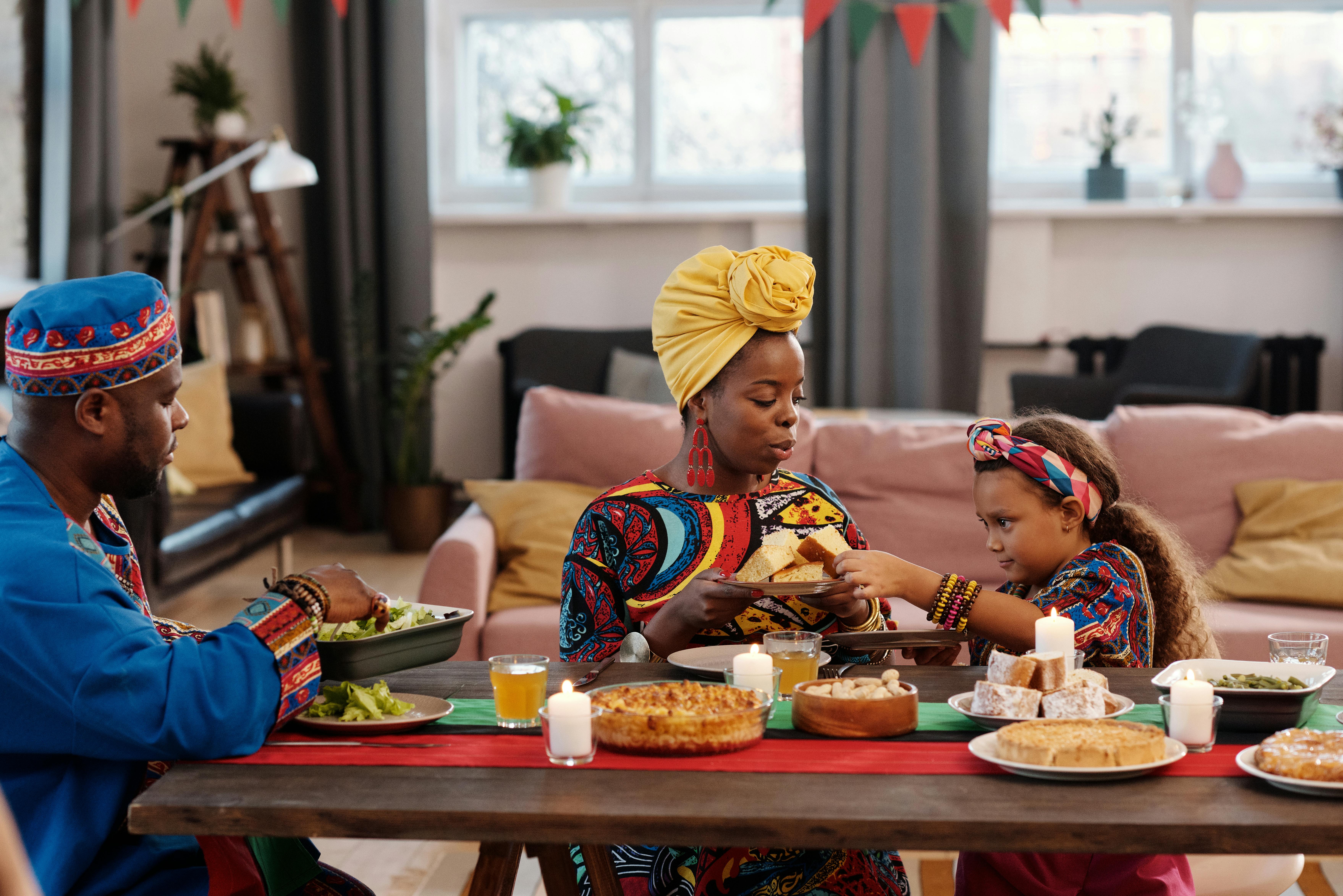 Home Family enjoying a Kwanzaa celebration with traditional clothing and foods in a cozy home setting.
