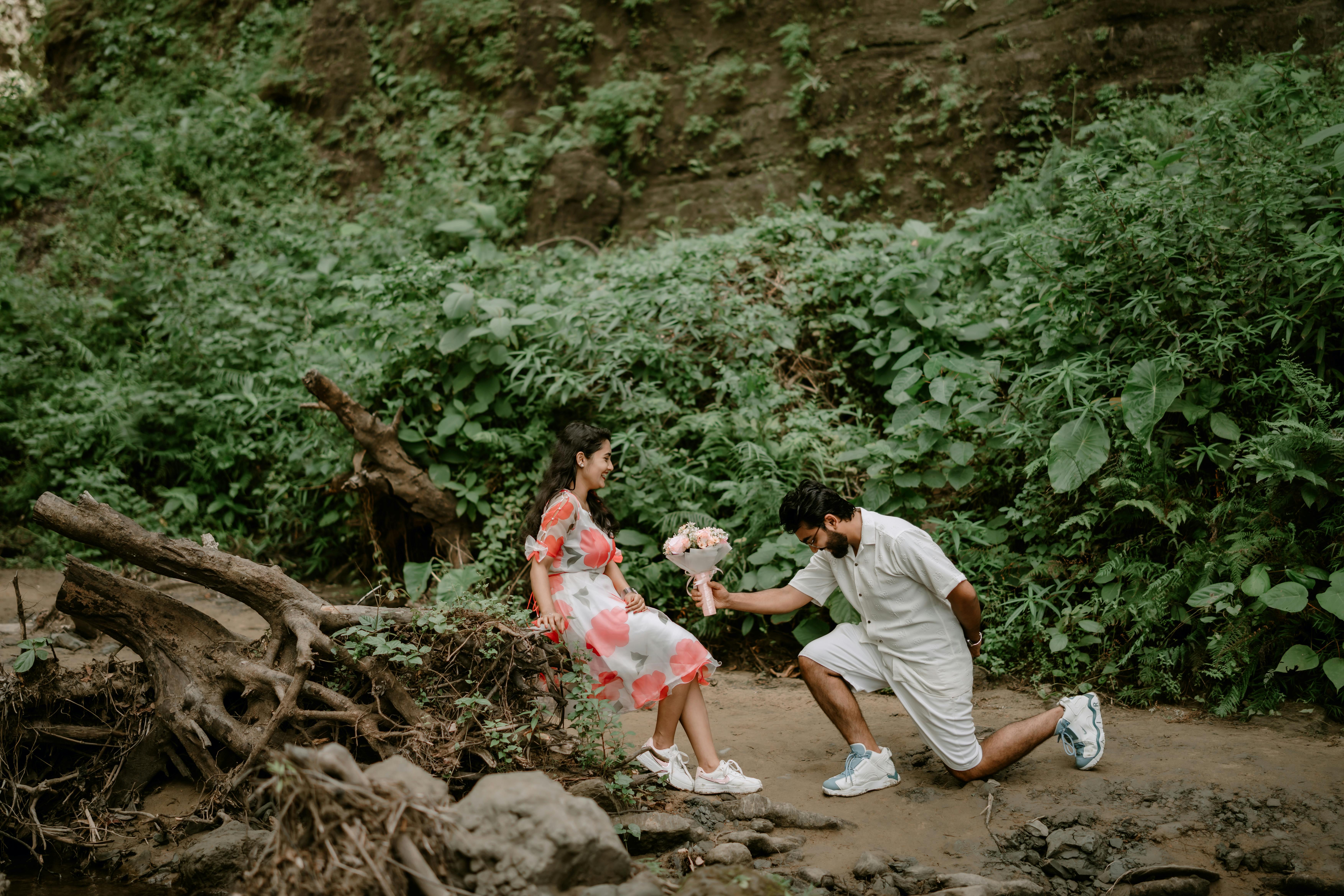 Home A romantic moment as a man proposes to a woman in a lush green outdoor scene.