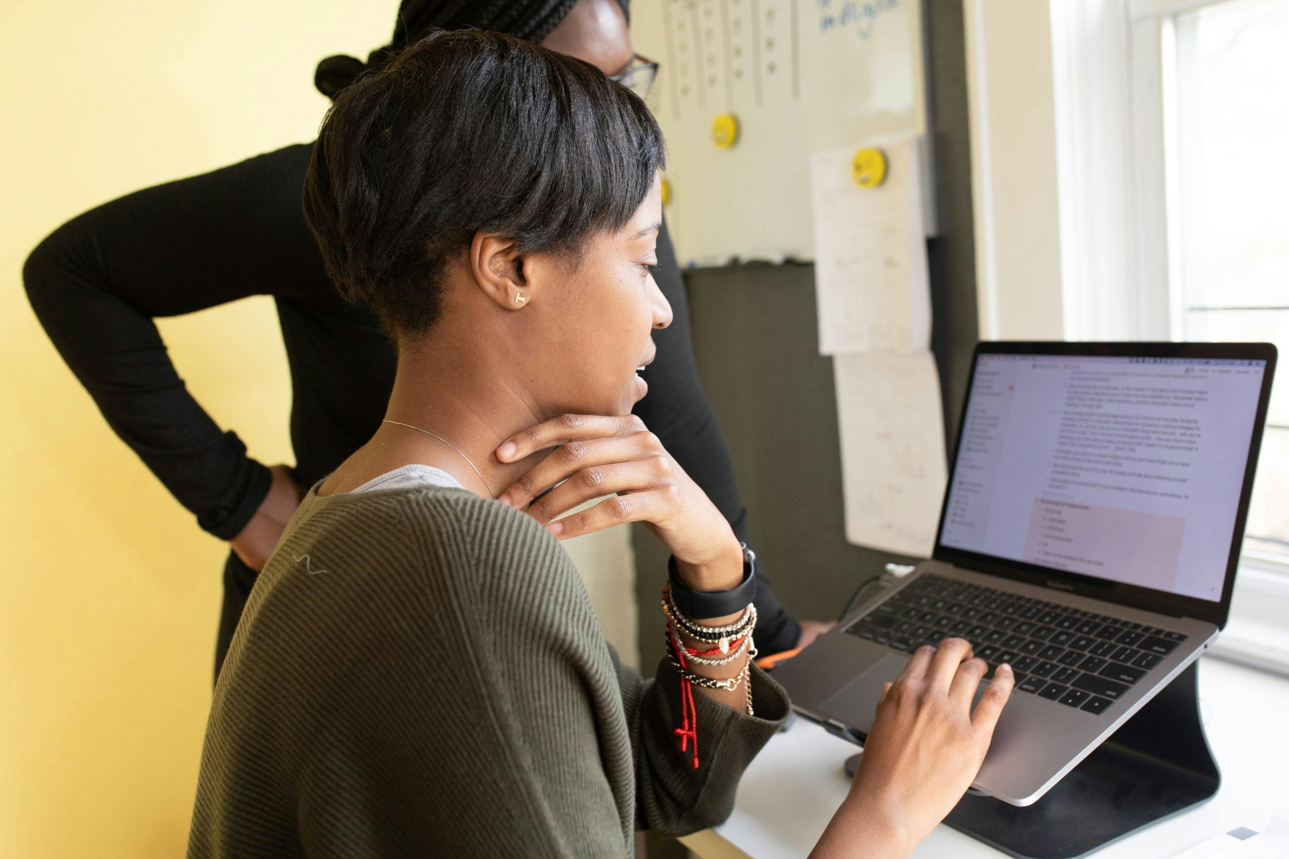 Services Two women working together on a laptop in an office environment, focusing on a project.
