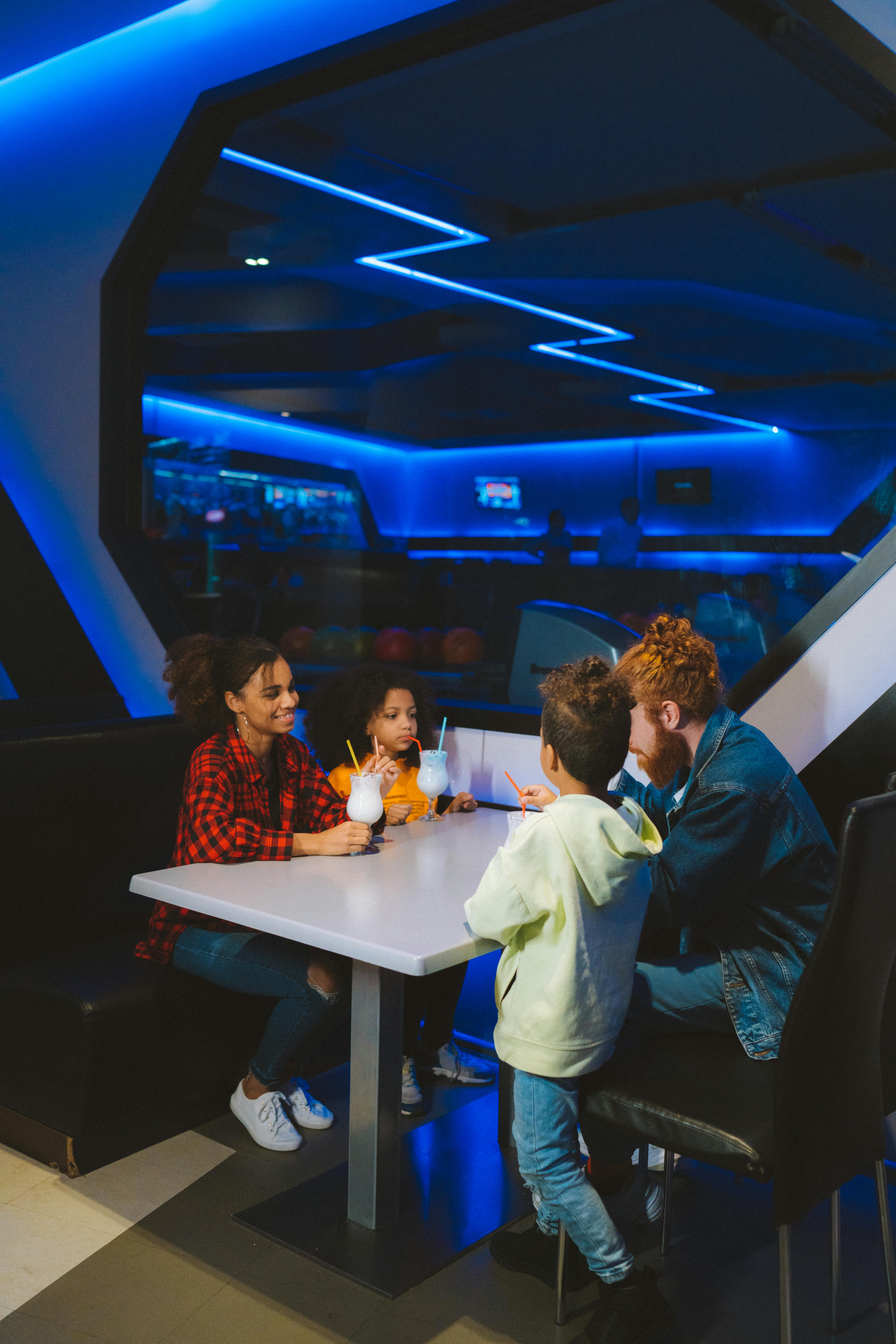 Home A family with children enjoying drinks at a table in a neon-lit restaurant setting.