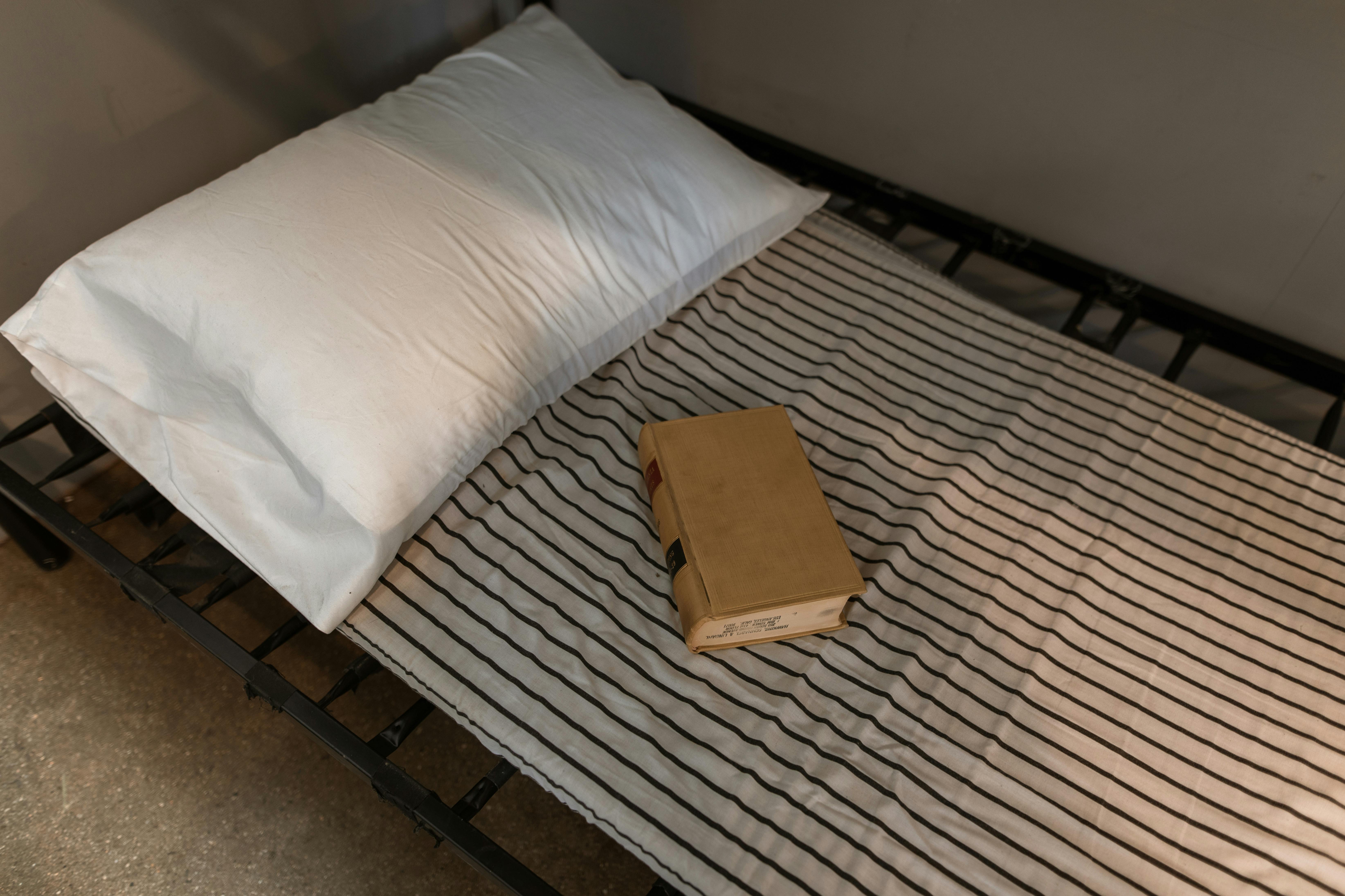 A cozy minimalist bed scene featuring a white pillow and a book on striped sheets.