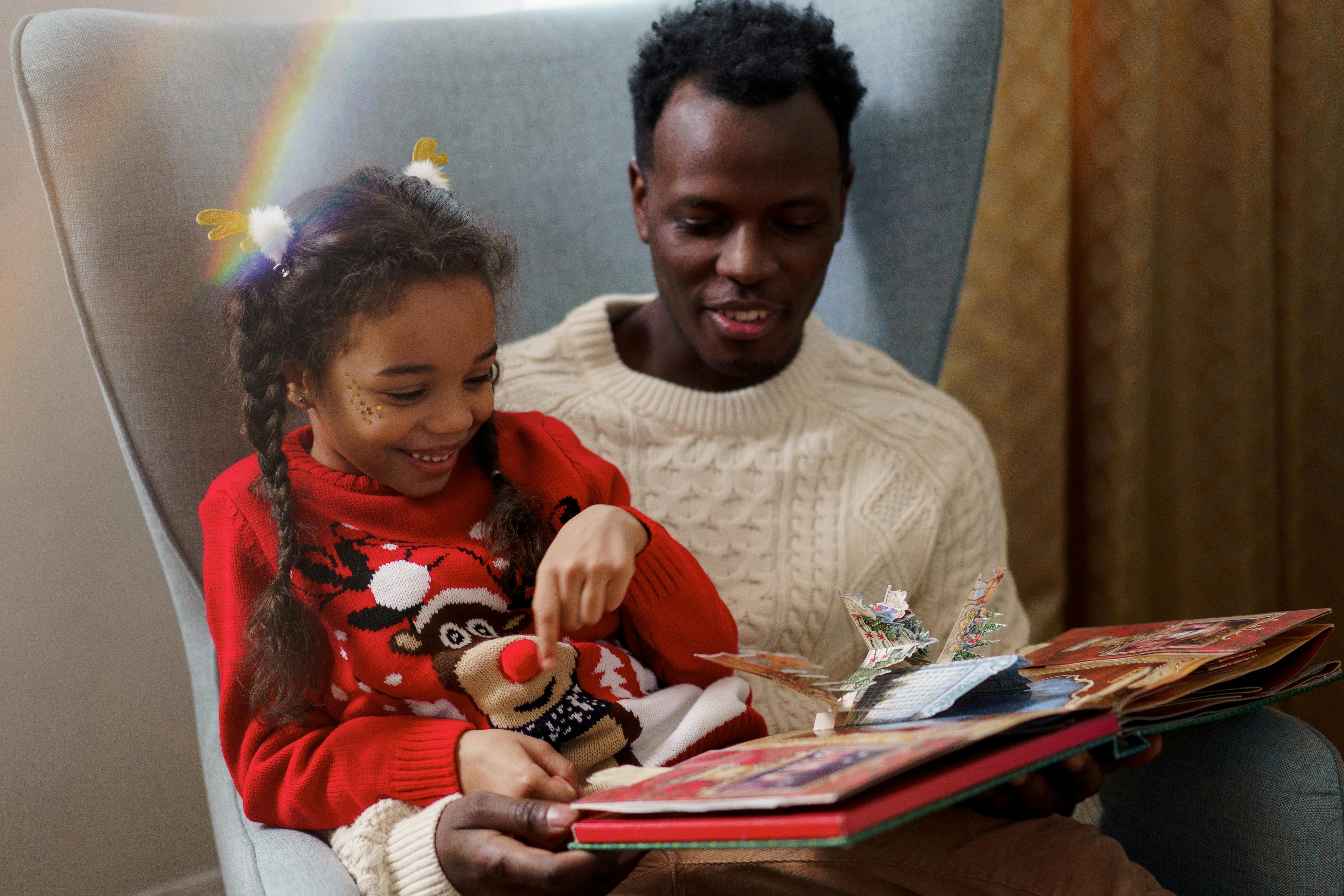 Home A father and daughter share a joyful moment reading a Christmas storybook indoors.