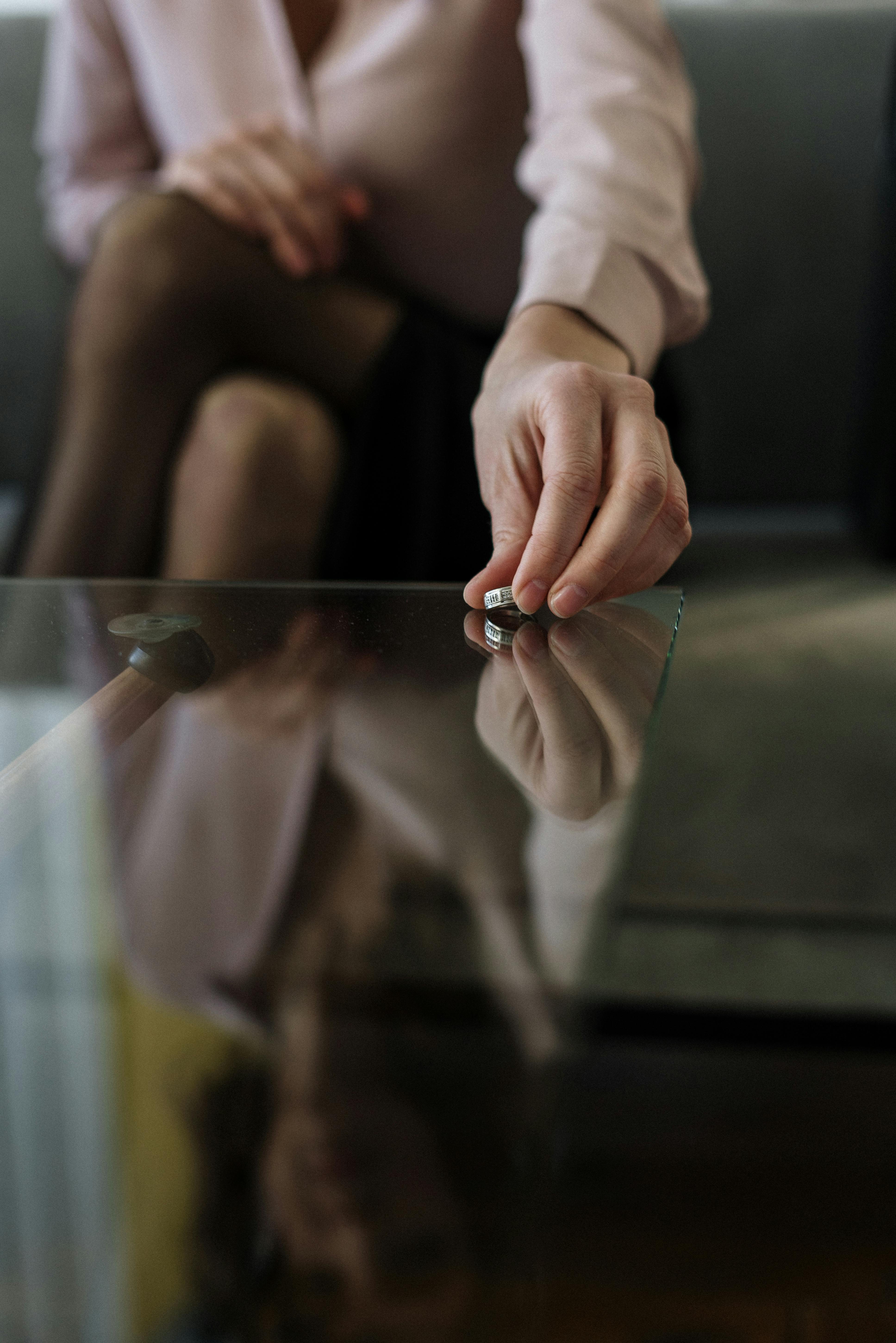 Home A person placing a wedding ring on a glass table, symbolizing separation or divorce.