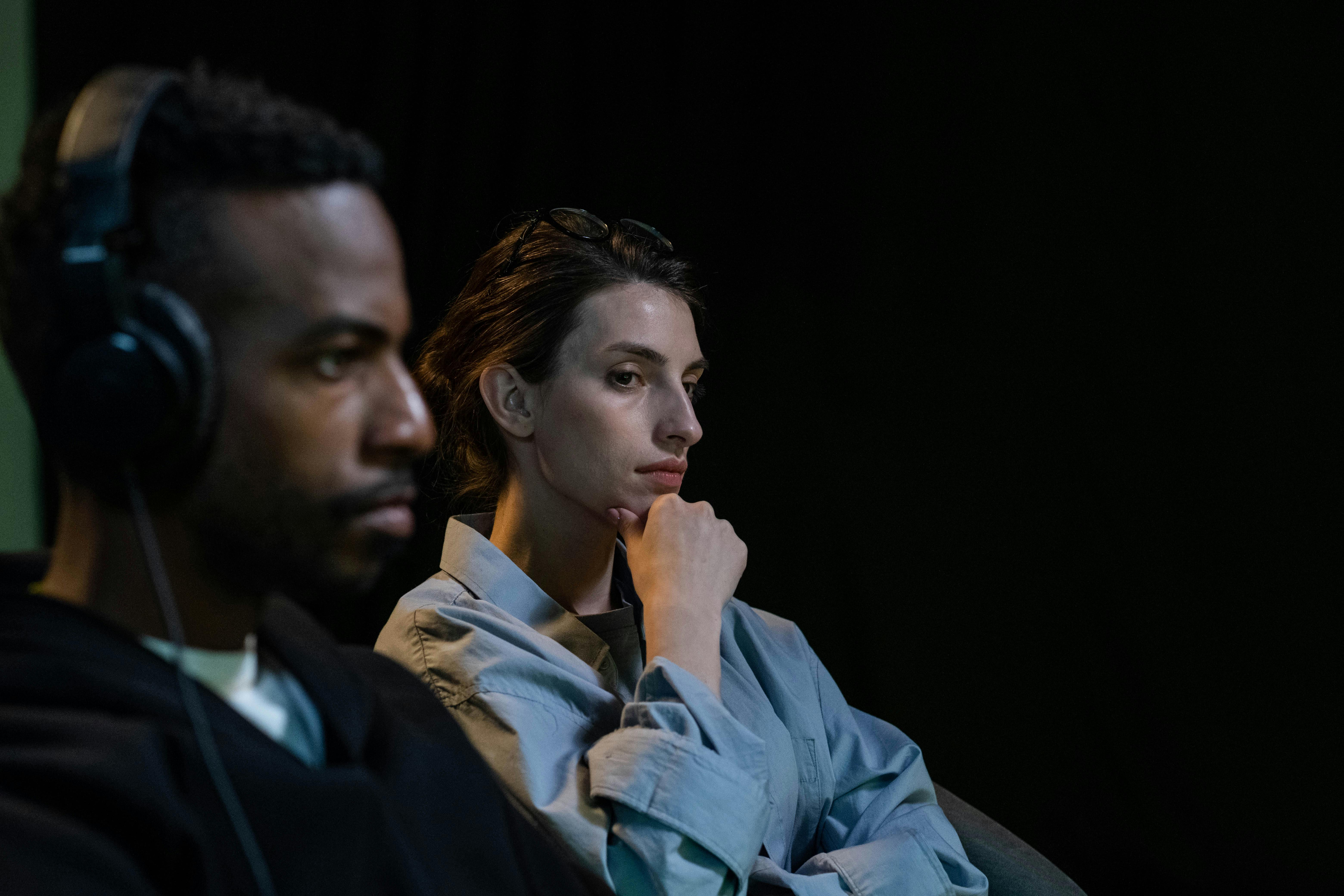 Two colleagues sitting with intense focus in a dark studio environment.