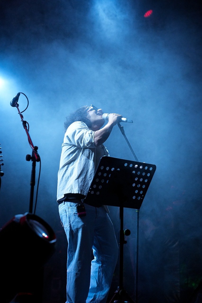 singer, microphone, stage lights, smoke, stage, concert, live music, musician, singing, artist, entertainment, live performance, concert stage, emotion, black shirt, energy, blues music, night, rock music