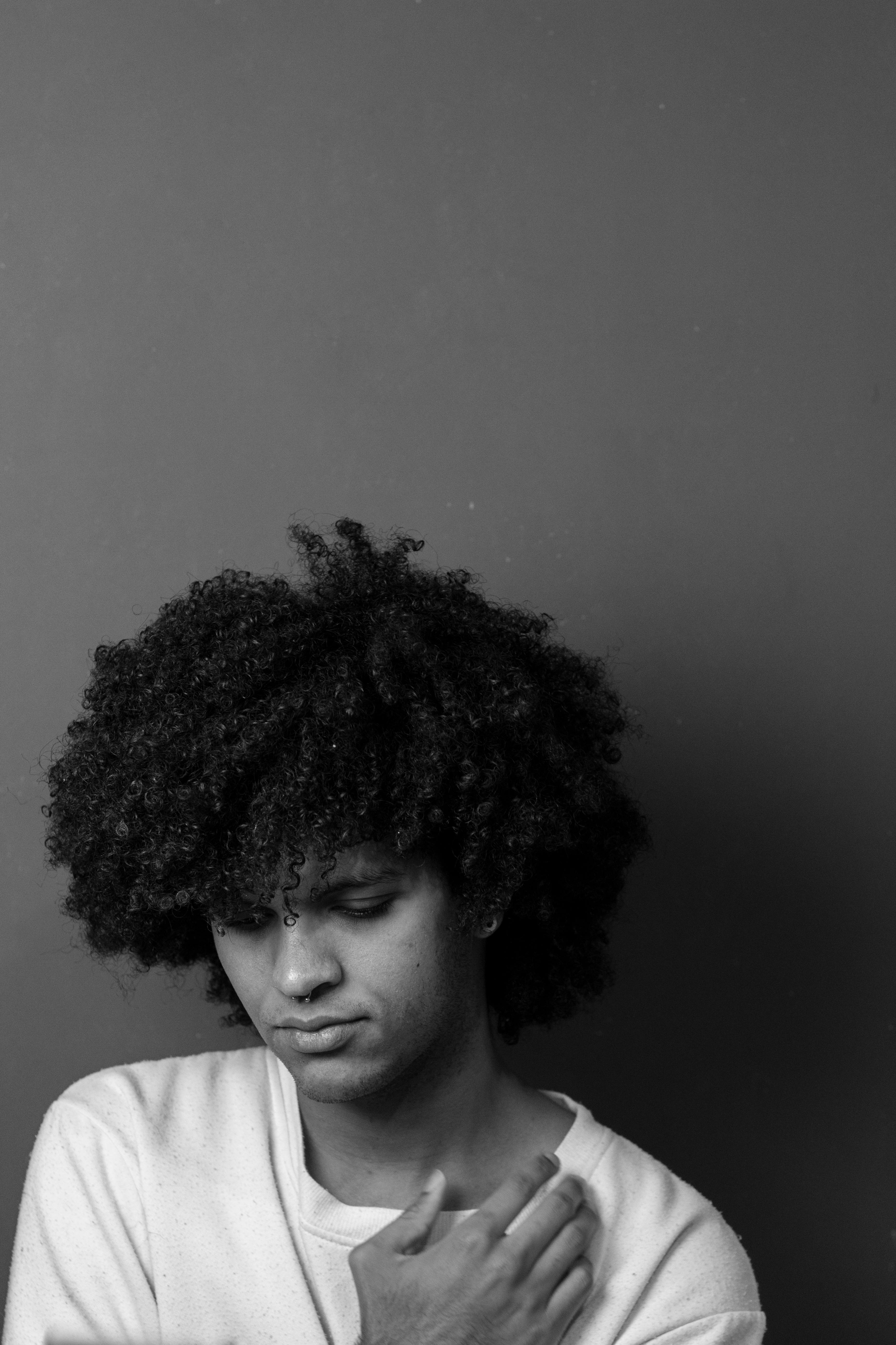 Black and white portrait of a young adult with afro hair, conveying emotion through subtle expression.