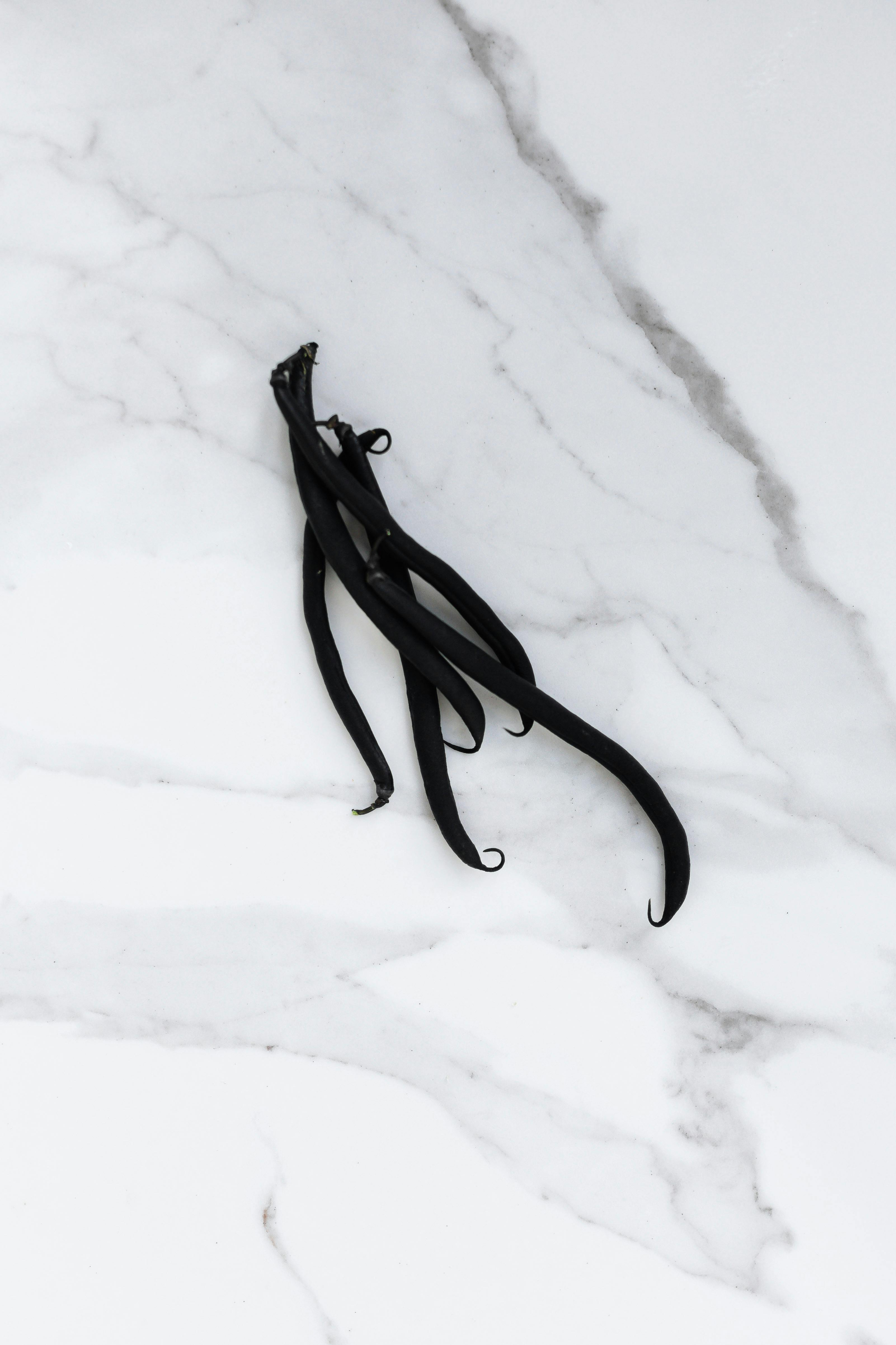High-angle view of vanilla beans displayed on a white marble surface, exuding elegance.