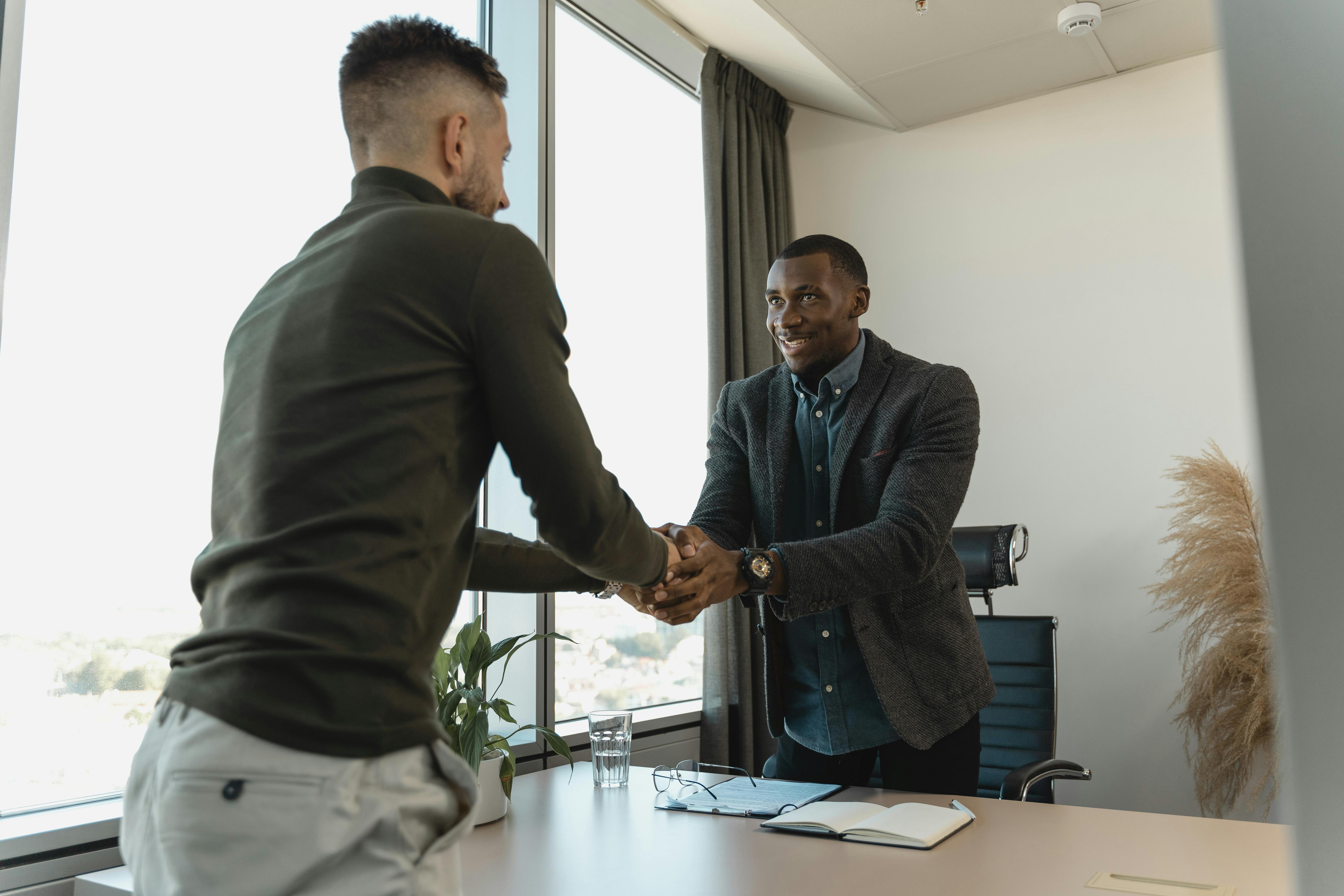 Services Two businessmen exchanging a handshake during a professional meeting in a modern office setting.