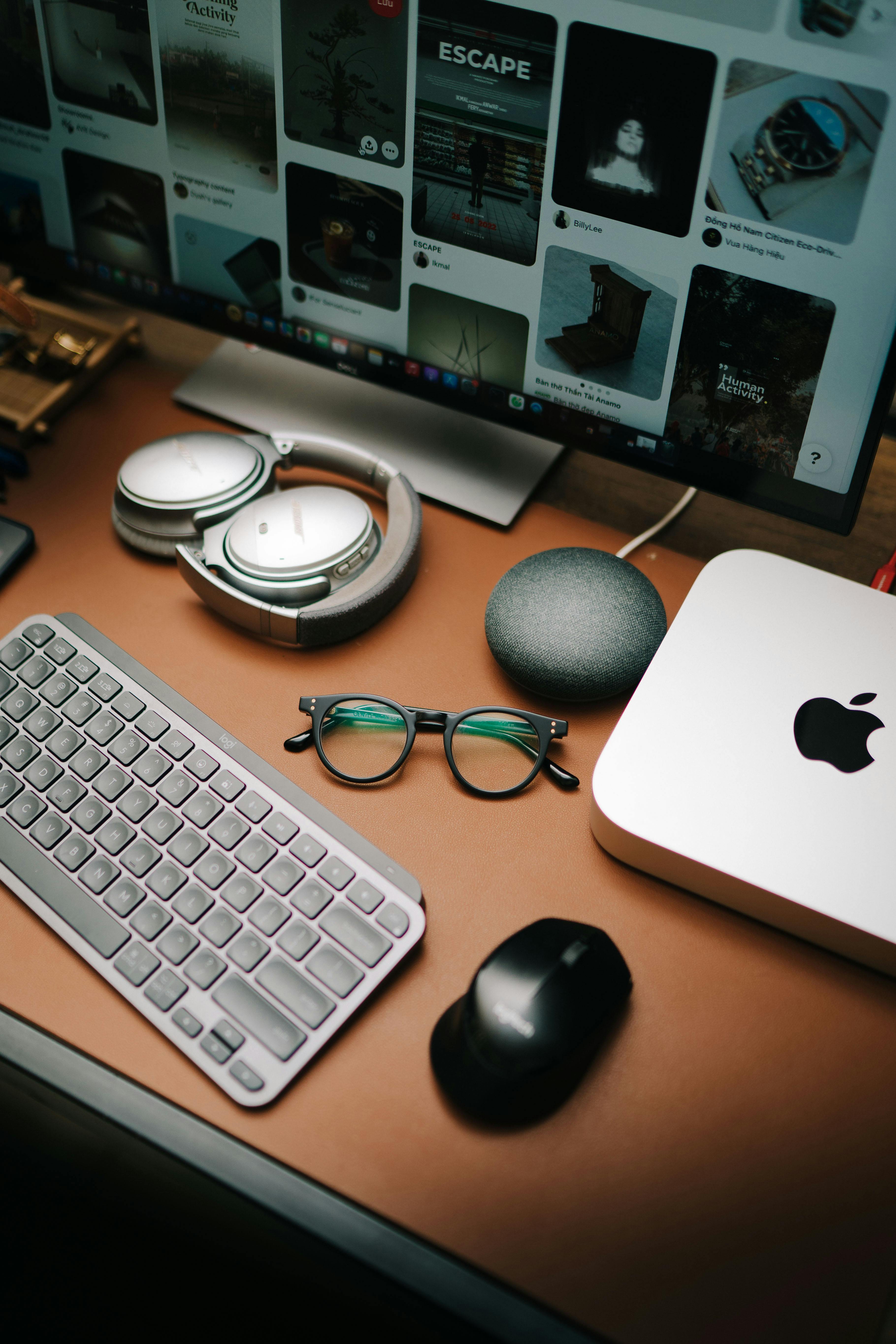 A stylish workspace featuring a keyboard, mouse, eyeglasses, headphones, and a screen displaying digital content.