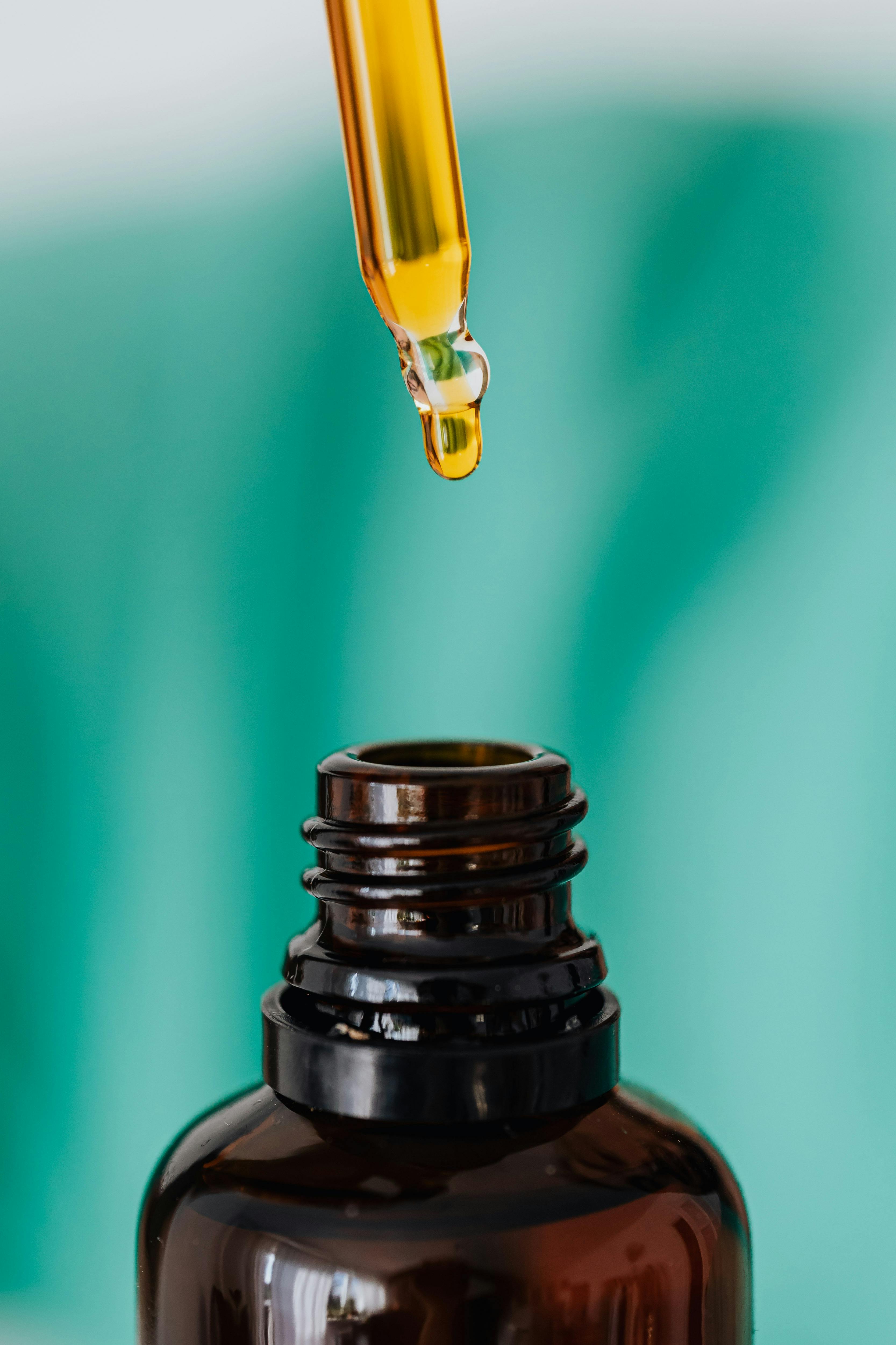 Services High-quality macro shot of dropper releasing liquid into glass bottle against green backdrop.