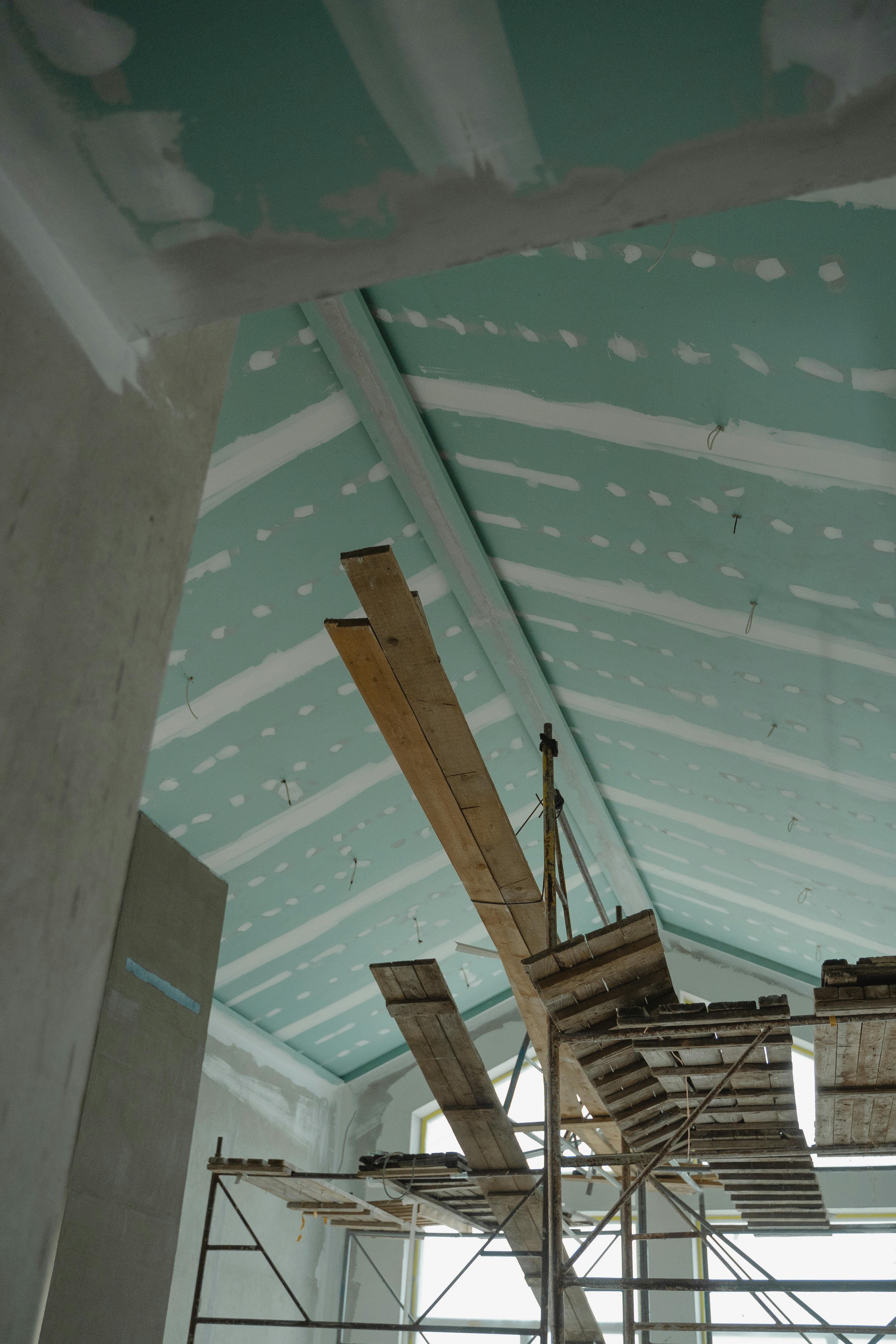 Scaffolding setup in an interior construction space with suspended ceiling boards and wooden planks.