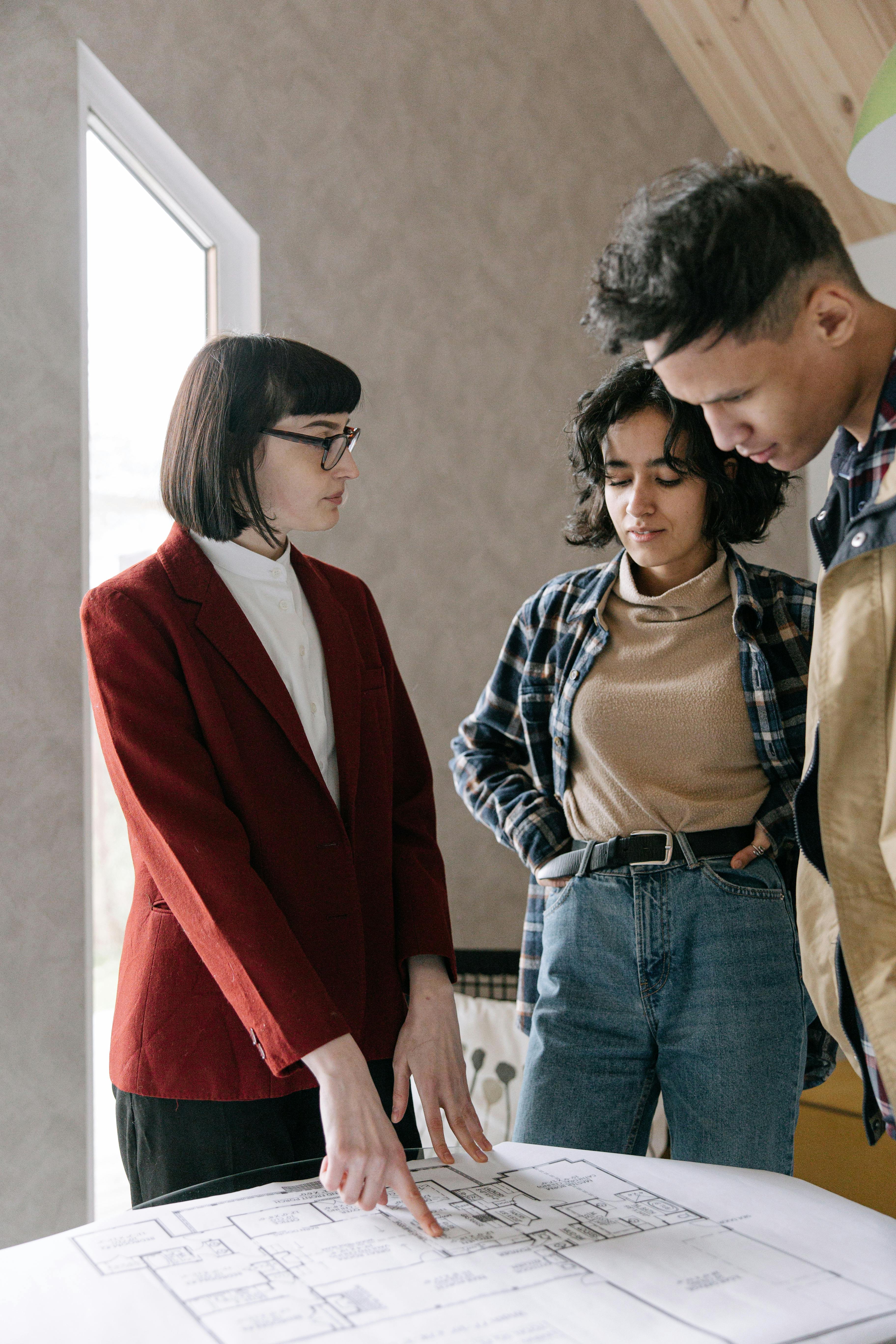 A real estate agent discusses home plans with a couple in a modern office setting.